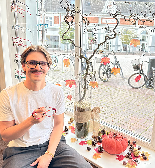 Mann mit Brille sitzt lächelnd in einem herbstlichen Fensterdisplay.