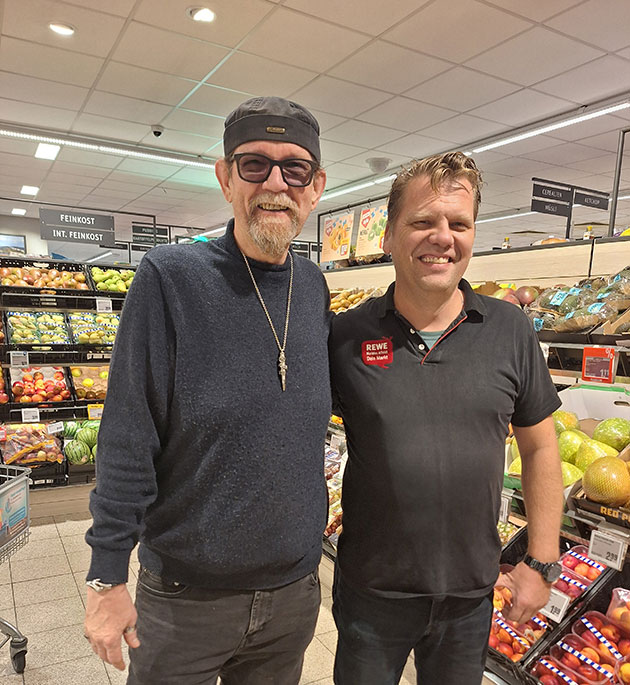 Zwei Männer in einem Supermarkt lächeln für ein Foto.