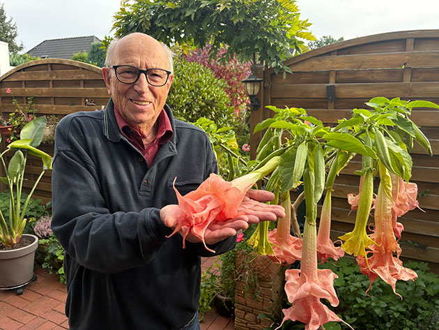 Mann hält große Blüten im Garten lächelnd in den Händen.