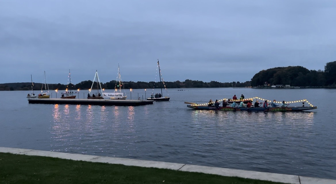 Boote mit Lichtern auf einem See am Abend.