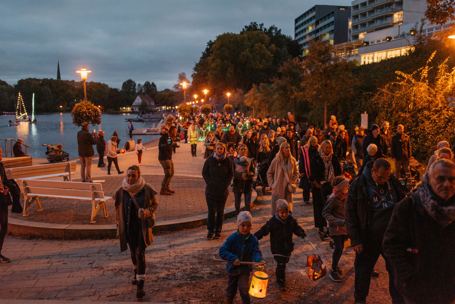 Menschen mit Laternen spazieren abends am Fluss.
