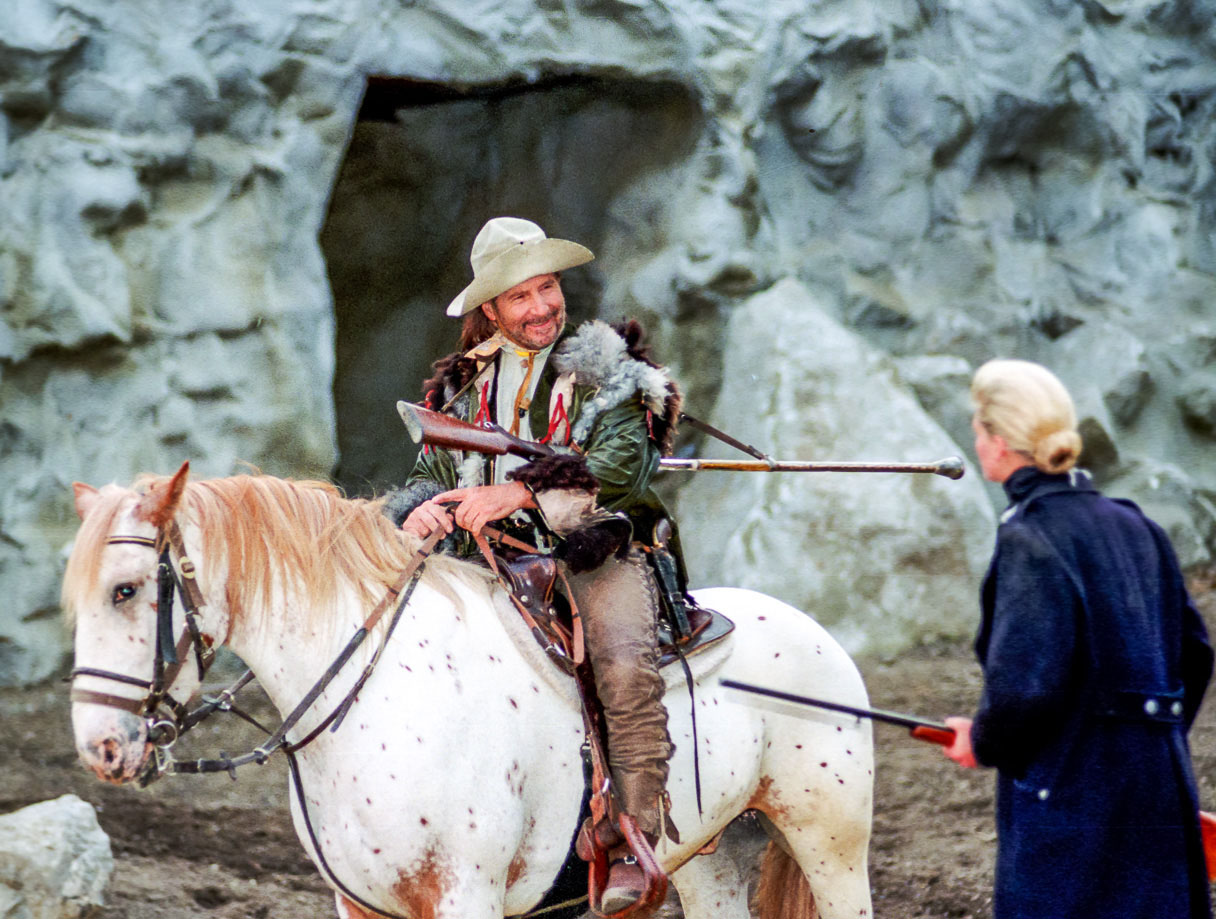 Mann auf Pferd in historischem Kostüm vor einer Höhle.