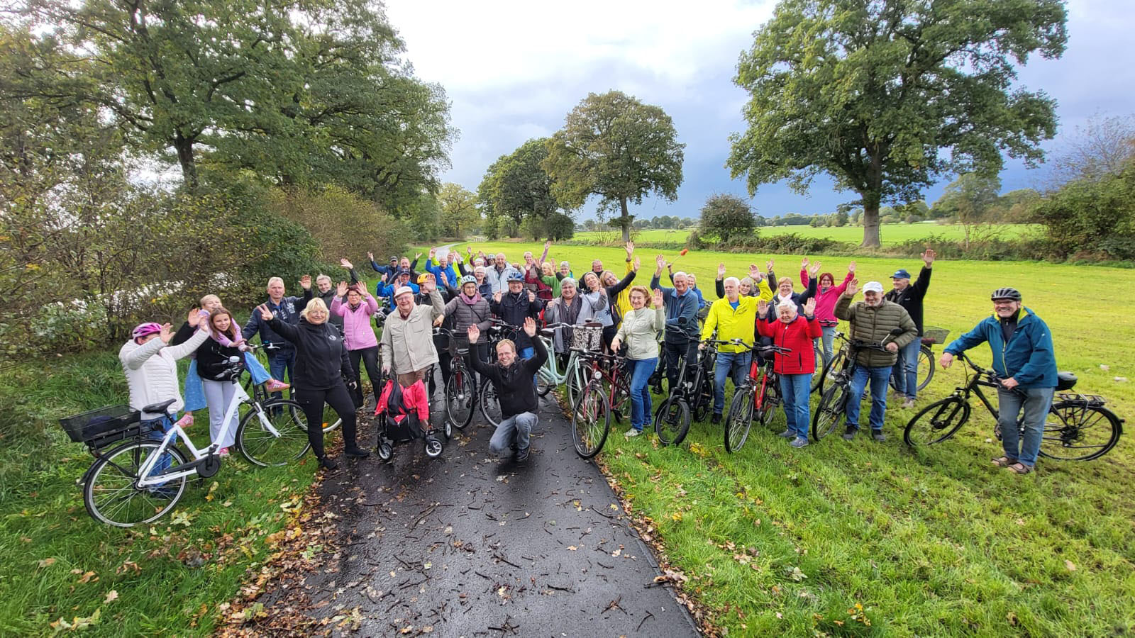 Gruppe von Radfahrern winkt auf einem Weg im Grünen.
