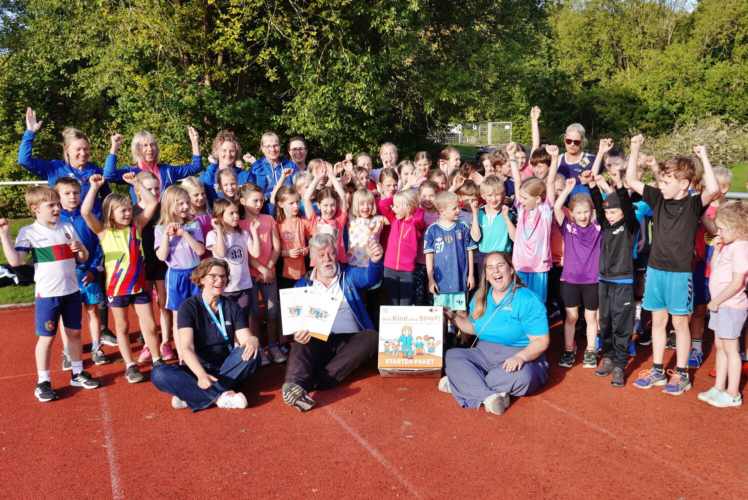 Gruppe von Kindern und Erwachsenen auf Sportplatz.