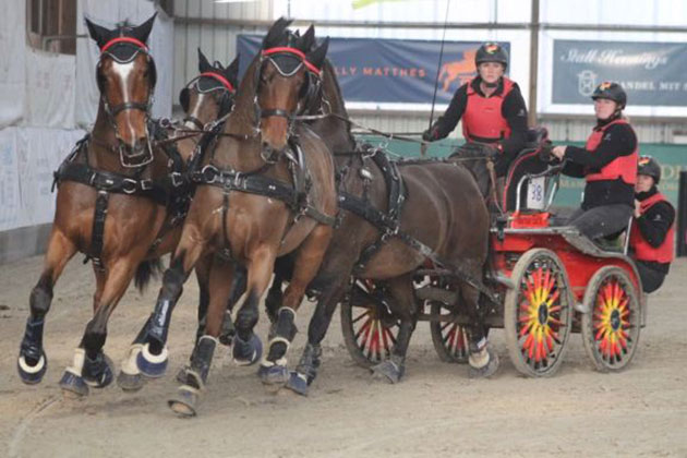 Kutsche mit vier Pferden und Fahrern in roter Kleidung.