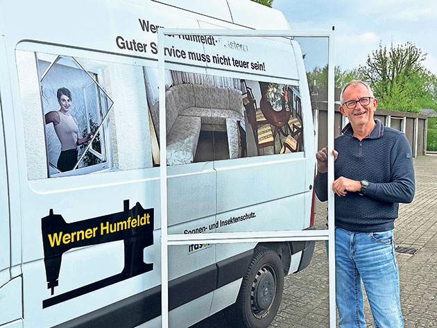 Mann steht neben einem Firmenwagen mit Text und Logo.