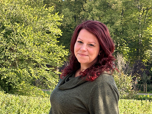 Frau im Freien vor einem grünen Hintergrund lächelt.