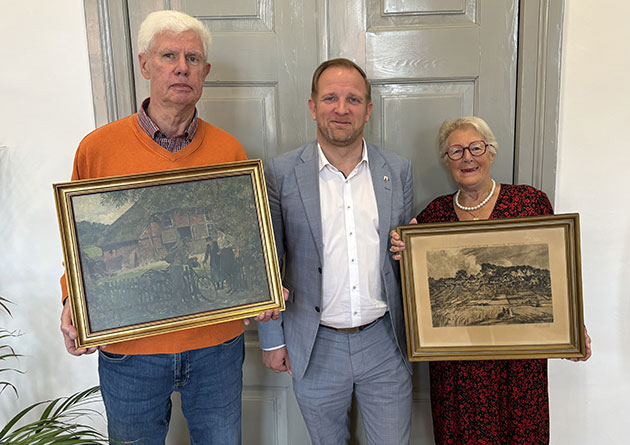Drei Personen halten gerahmte Bilder vor einer grauen Tür.