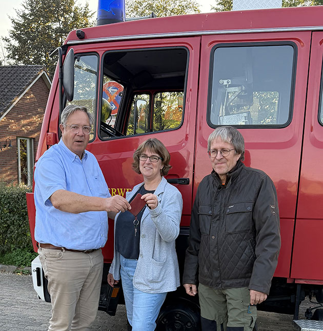Drei Personen stehen vor einem roten Feuerwehrwagen.