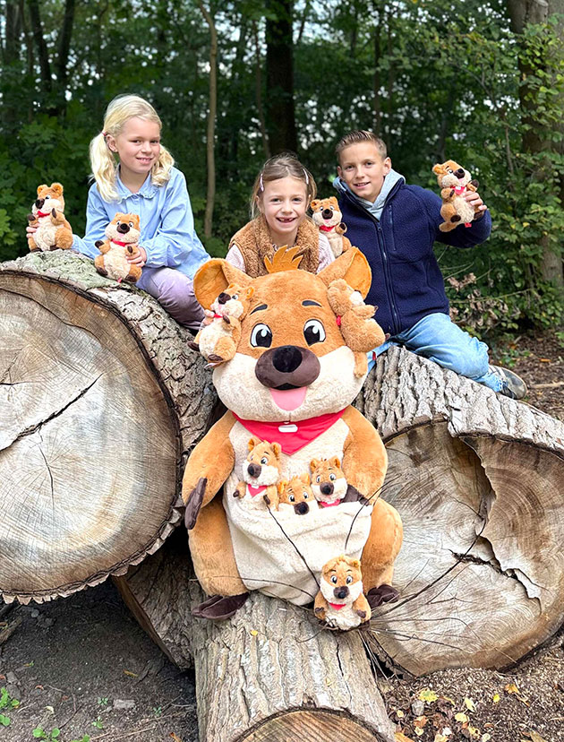 Kinder sitzen mit Kuscheltieren auf Baumstämmen im Wald.