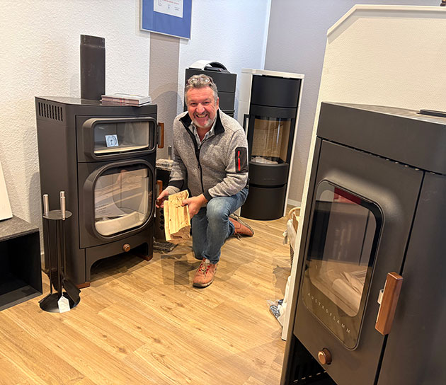 Mann mit Brennholz vor Kaminofen im Showroom