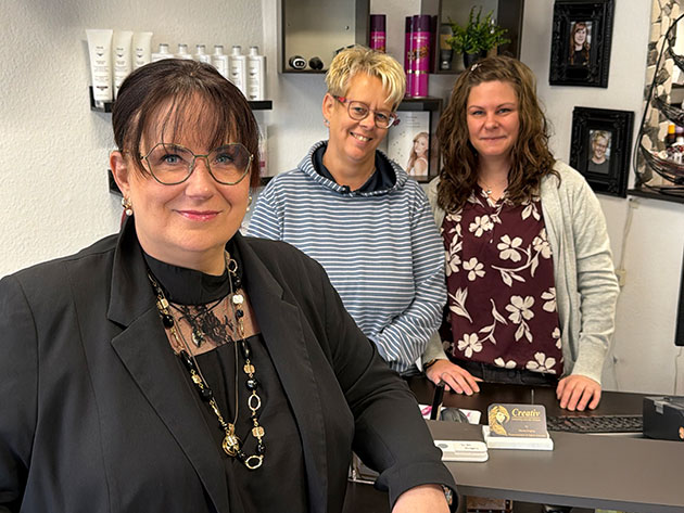Drei Frauen in einem Friseursalon, lächelnd in die Kamera.