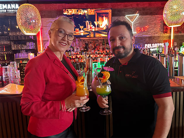 Zwei Personen halten Cocktailgläser in einer Bar.
