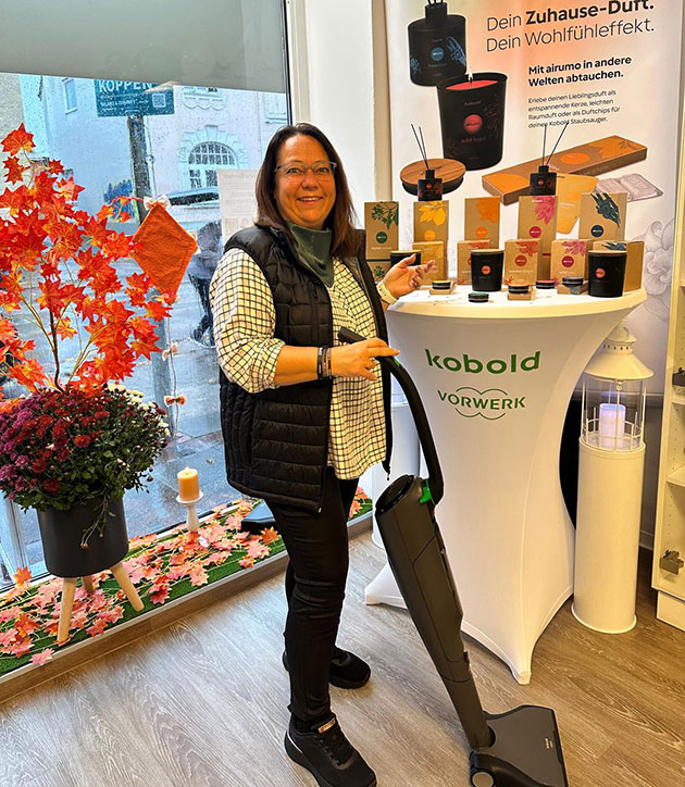 Frau mit Staubsauger neben Duftproduktpräsentation im Laden.