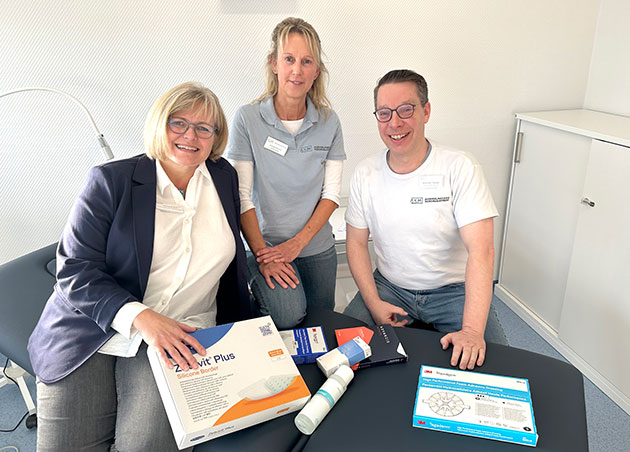 Drei Personen mit medizinischen Produkten am Tisch.