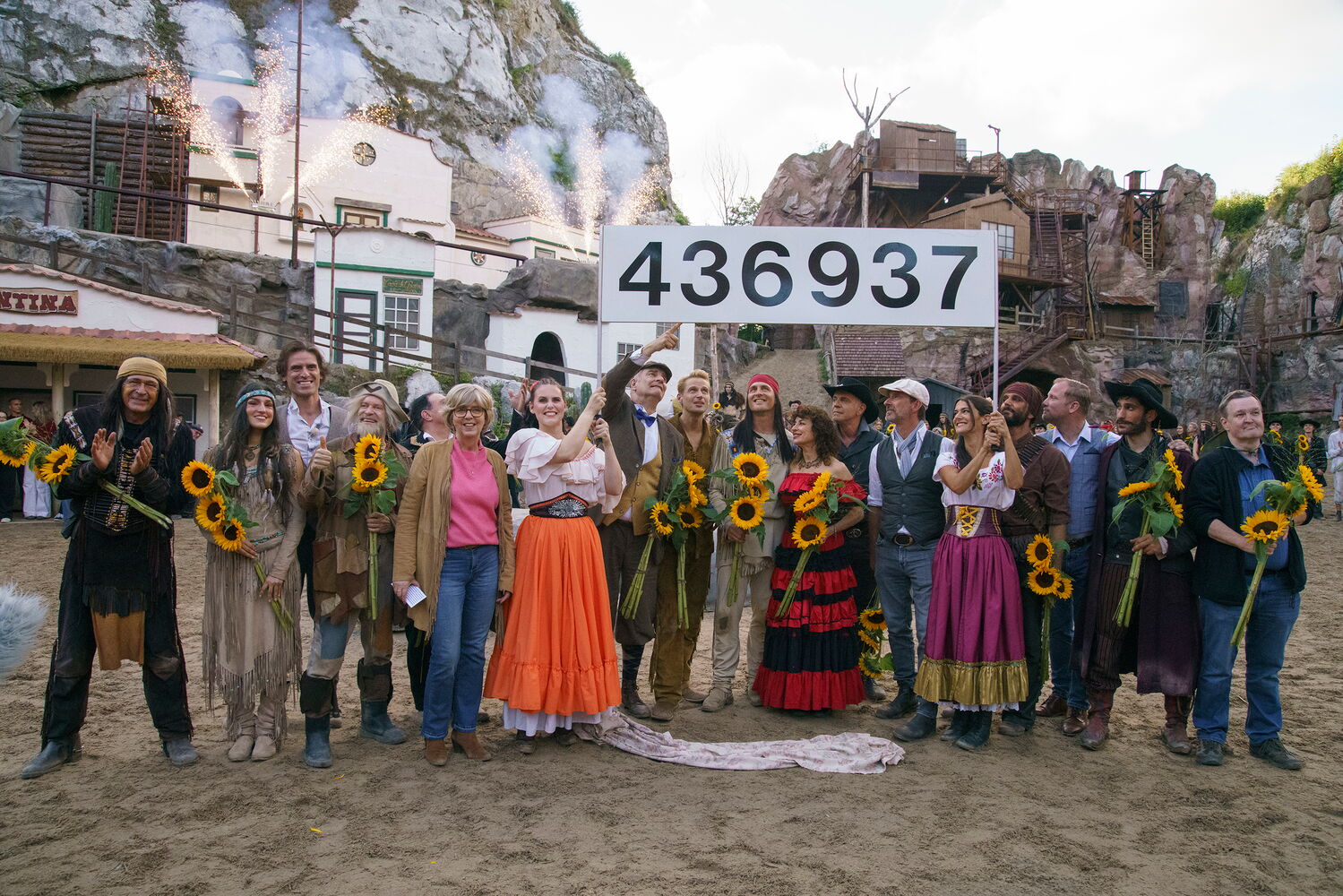 Gruppe posiert vor Kulisse mit Sonnenblumen und großer Zahl 436937.