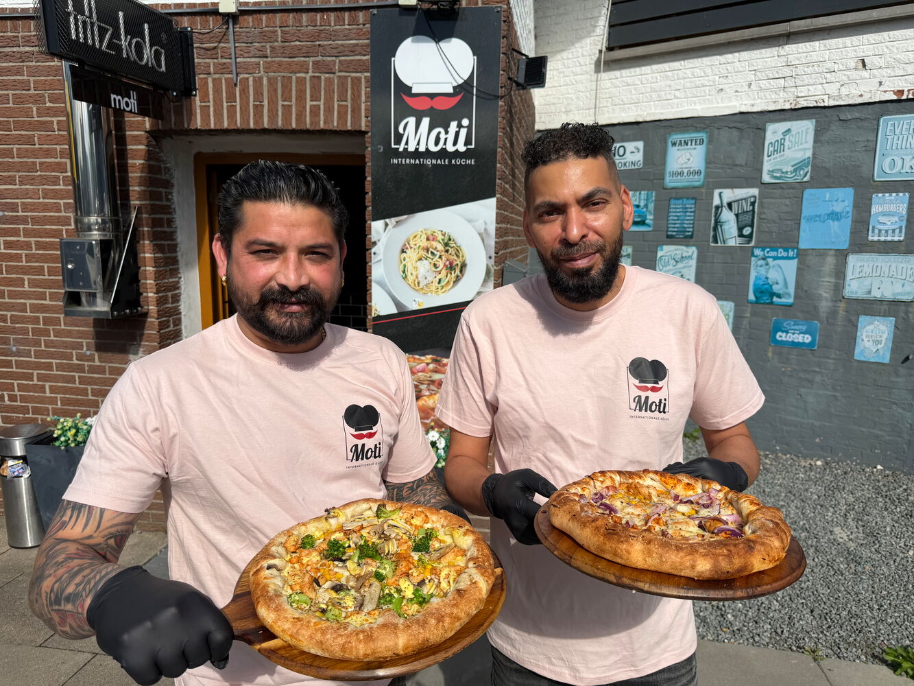 Zwei Männer halten Pizzen vor einem Restaurant.